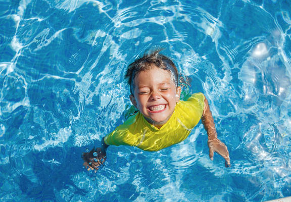 boy floating in bright blue swimming pool