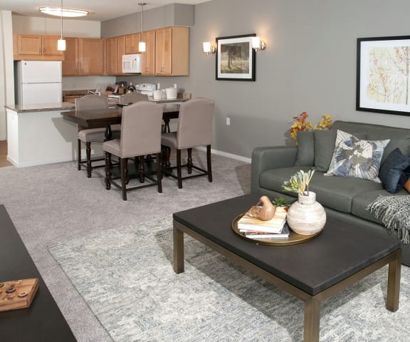 a living room with a couch coffee table and a kitchen in the background at The Legends of Columbia Heights 55+ Living, Columbia Heights, MN