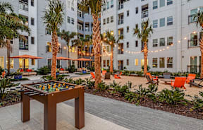A table tennis table is in the middle of a courtyard with palm trees and apartment buildings in the background.