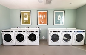 A laundry room with a row of washing machines and pictures on the wall.