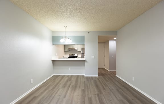 an empty living room with a kitchen in the background