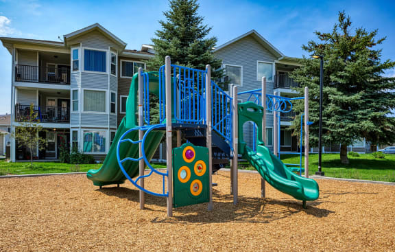a playground with a play set and slides in front of an apartment building