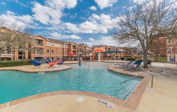 a swimming pool with chairs and umbrellas in front of a buildingat Stoneridge Apartments, Pflugerville Texas