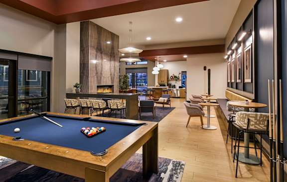 A pool table is in the middle of a room with a bar and chairs.