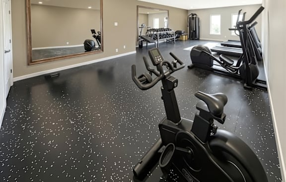 A black exercise bike is in the foreground of a spacious gym with a mirror and other exercise equipment.