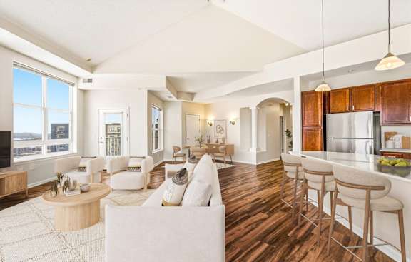 A spacious living room with white furniture and a large window overlooking the city.