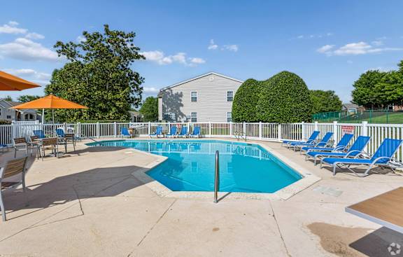 A pool surrounded by chairs and trees with a building in the background.