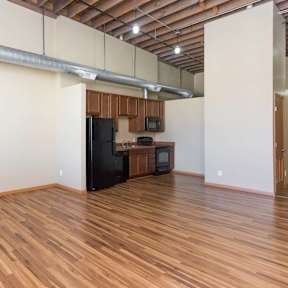 A kitchen area with wooden floors and a black refrigerator.at Riverpoint Lofts, Iowa, 50309