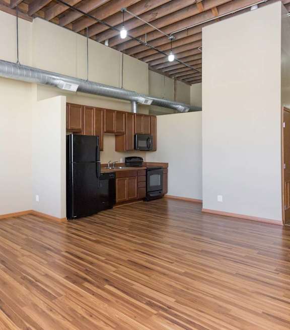 A kitchen area with wooden floors and a black refrigerator.at Riverpoint Lofts, Des Moines, IA
