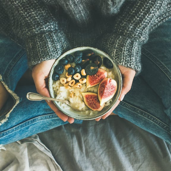 a woman sitting on a bed holding a bowl of cereal and fruit at Salish Flats APARTMENTS, Airway Heights, WA 99001