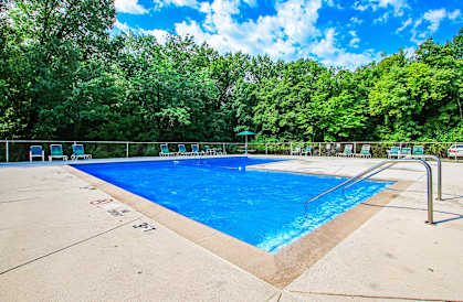 a swimming pool with chairs around it and trees in the background