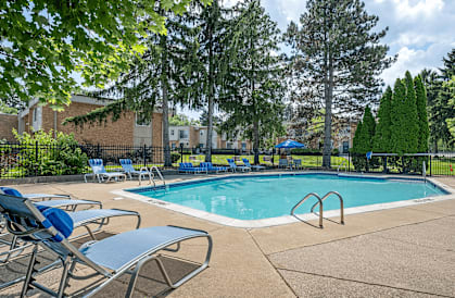 A pool surrounded by trees and chairs.