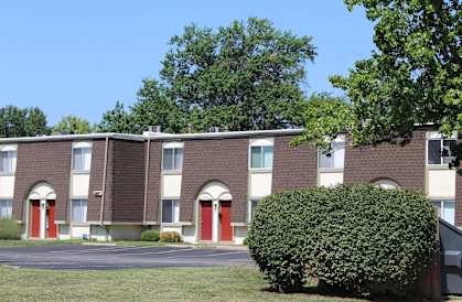 A building with red doors and windows is surrounded by greenery.