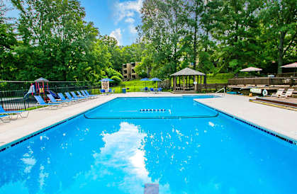 a swimming pool with chairs around it and trees in the background