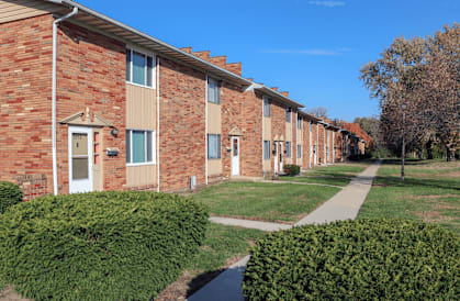 A row of red brick houses with green bushes in front.