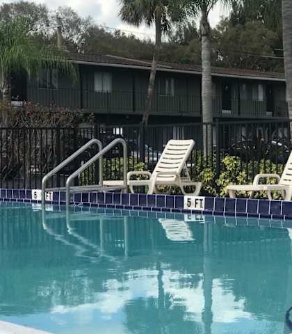 swimming pool with lounge chairs in front of apartment buildings and palm trees