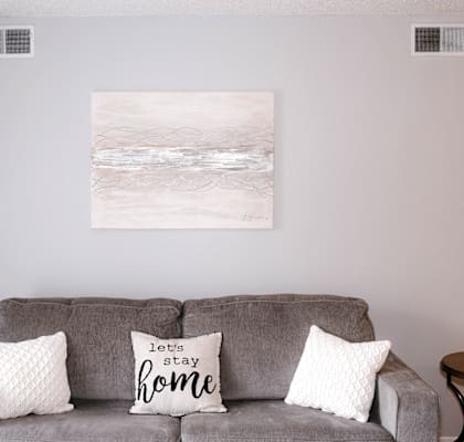 A grey couch with two pillows and a sign that says "let stay home".