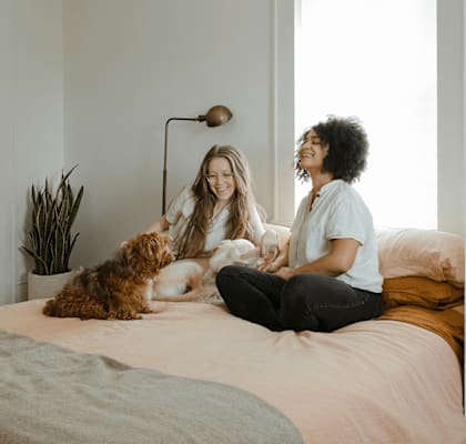 Two women sitting on a bed with a dog.