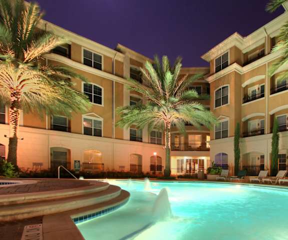 A swimming pool in front of a building with palm trees.