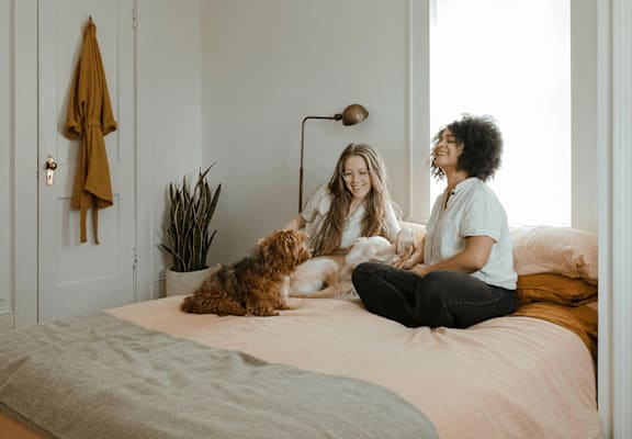 Two women sitting on a bed with a dog.