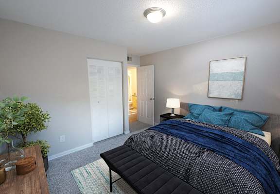 A bedroom with a bed, nightstand, and a plant.