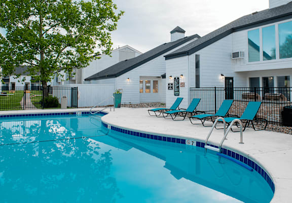 a swimming pool with blue chaise lounge chairs and a white building in the background