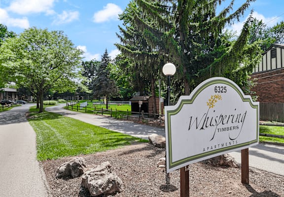 a street sign in front of a park with trees and a path