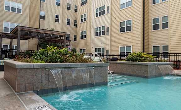 A pool with a waterfall in front of apartment buildings.