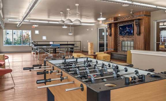 A foosball table is in the middle of a room with a brick wall and a TV.