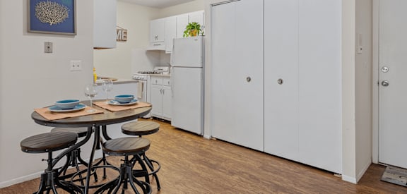 a dining area with a table and four stools next to a kitchen with a refrigerator and