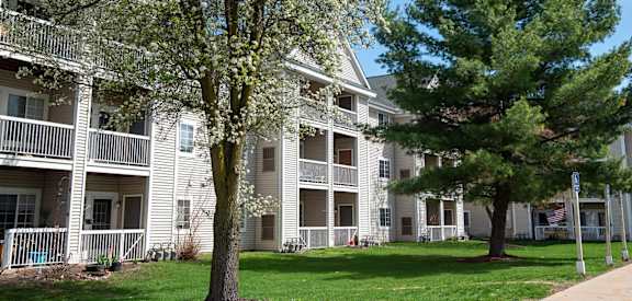A tree with white blossoms stands in front of a building with a white balcony.