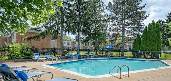 A pool surrounded by trees and chairs.