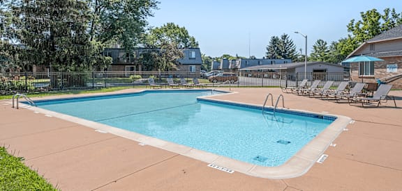 A large outdoor swimming pool surrounded by a fence and lounge chairs.