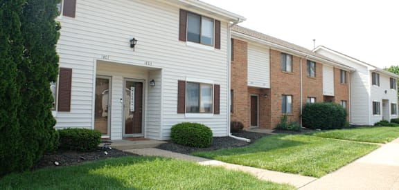 a white and brick apartment building with a sidewalk in front of it