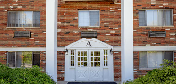 A white door with a black mat in front of a brick building.