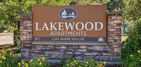 A sign for Lakewood Apartments is displayed in front of some trees and flowers.