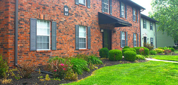 a red brick building with green grass and bushes in front of it