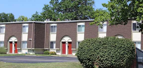 A building with red doors and windows is surrounded by greenery.