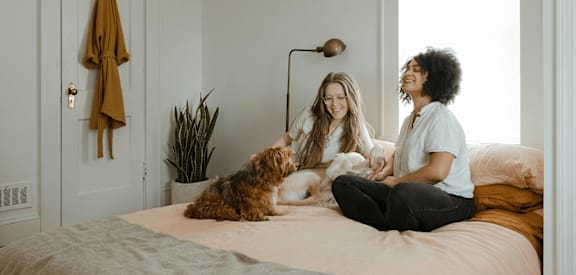Two women sitting on a bed with a dog.