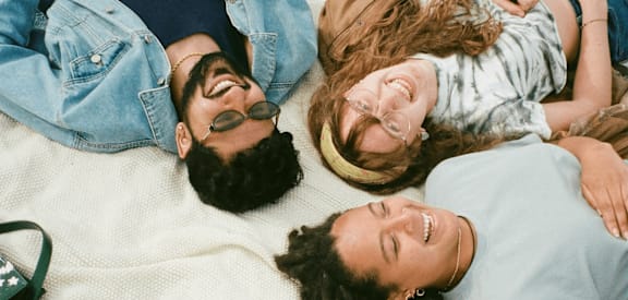 Three people are lying down on a white blanket.