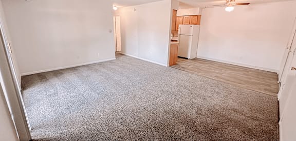 an empty living room with a kitchen in the background