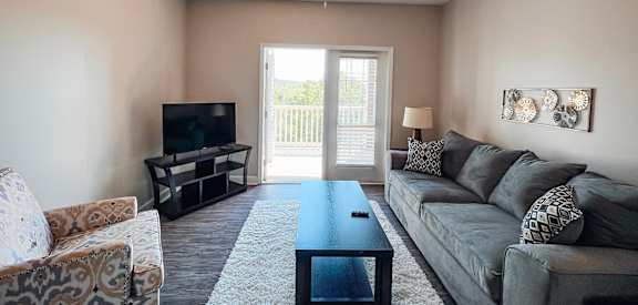 A living room with a grey couch, a coffee table, a television, and a ceiling fan.