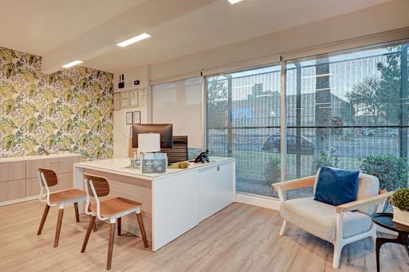A kitchen with a white counter and chairs with a view of the outside.