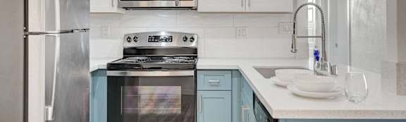 A kitchen with a stainless steel refrigerator, a black stove, and white cabinets.