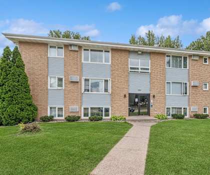 a brick apartment building with a green lawn and a sidewalk