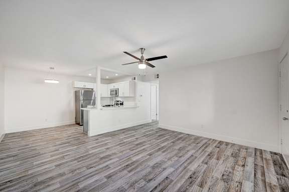 A room with a ceiling fan and a kitchenette in the background.