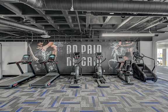 A gym with treadmills, elliptical machines, and a wall mural.