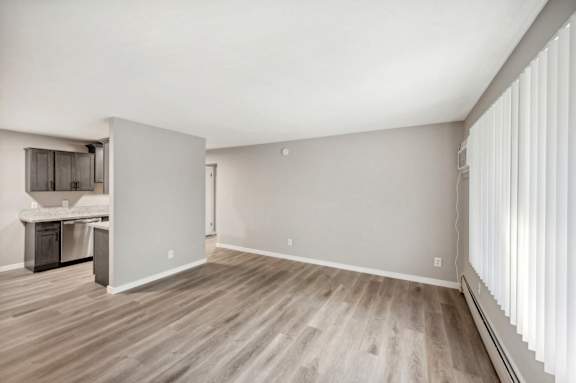 the living room of an apartment with wood flooring and a kitchen