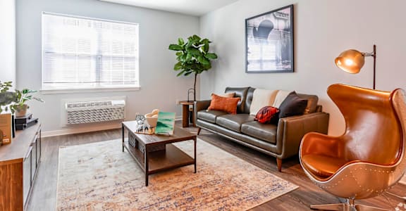 A living room with a brown leather couch, a wooden coffee table, and a large window.