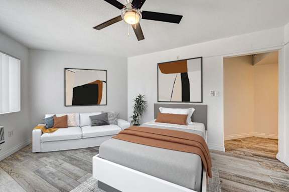 A bedroom with a bed, couch, and a ceiling fan.